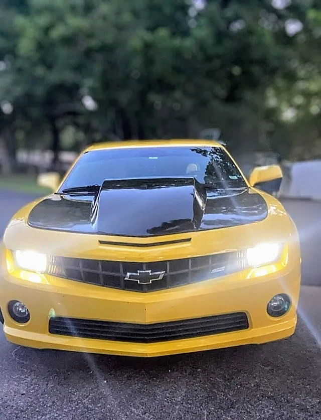 A yellow car with black hood stripes, seen from the front.