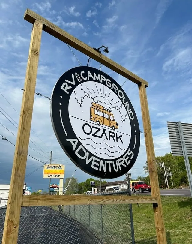 A round campground sign hung from a timber frame beside the road.