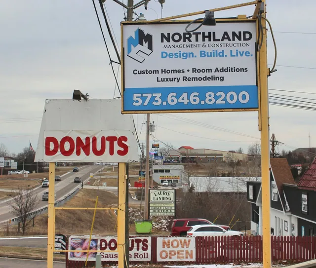 A pole-mounted business sign with a logo and phone number beside the road.