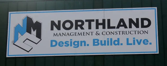 A wall-mounted business sign with a logo on a dark metal building.